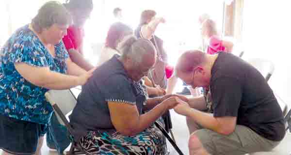 Ann Wheeler, standing at left, and Vaughn Wheeler, seated at right, pray with a recipient at Thursday's food give away organized by New Beginnings Worship Center and volunteers.